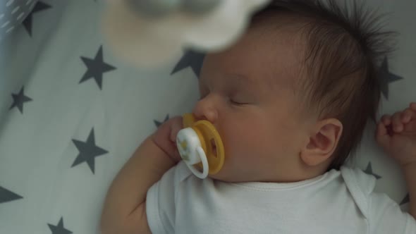 Handsome Little Boy Sleeping Sweetly in His Crib. Infant Sucks a Pacifier and Falls Asleep Under a