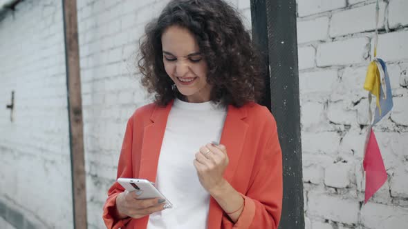 Excited Young Woman in Elegant Clothing Expressing Positive Emotions Looking at Smartphone Screen