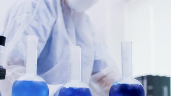 Female Scientist Holding and Looking at a Blue Solution with Reagent in Research Laboratory