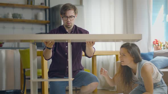 Married Couple Assembling Cabinet Together Sitting On Floor Indoors