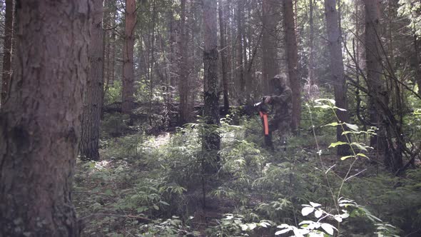 Hunter in Camouflage Aims Gun at Object in the Forest in Summer. Man Hunter Takes Aim with Rifle