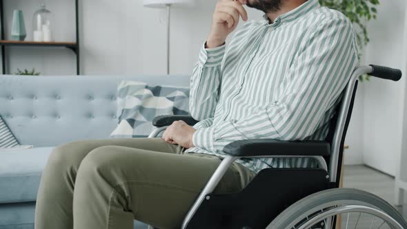Portrait of Lonely Disabled Guy Sitting in Wheelchair with Sad Face Thinking Indoors at Home