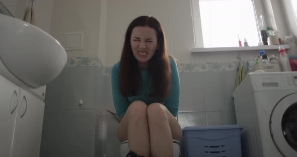 Female Sitting In A Toilet Expressing Pain