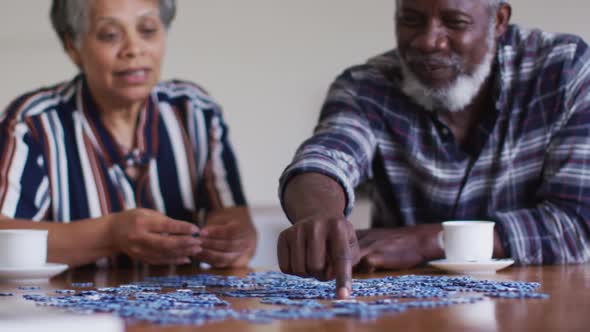 African american senior couple sitting by table doing puzzles drinking tea