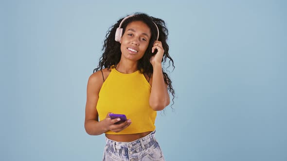 Afroamerican Girl is Choosing a Song on Her Mobile Phone and Listening It Through Headphones