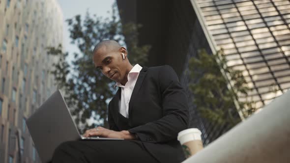 Positive African businessman working on laptop in headphones