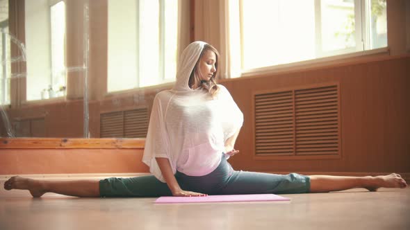 Young Pretty Woman Sitting on the Yoga Mat Performing a Split - Doing Leg Stretching Exercises -