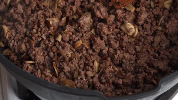 Motion Over Black Frying Pan on Gas Stove with Beef with Onion Mushrooms and Wooden Spatula