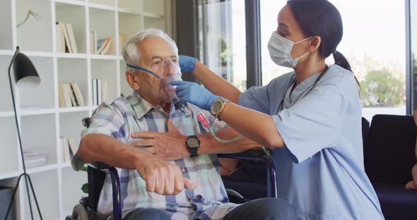 Video of biracial female doctor in face mask keeping oxygen to caucasian senior man