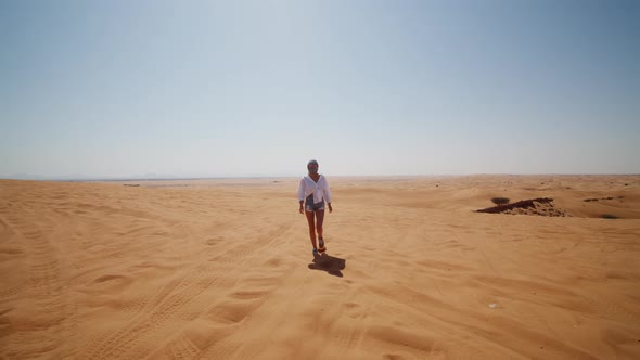 Front View of Young Woman in Sunglasses and Scarf Over Her Head Walking in the Desert Near Dubai