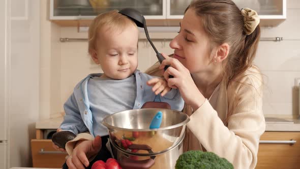 Happy Smiling Mother Playing with Ladle and Her Baby Son While Cooking on Kitchen