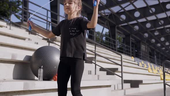 Sporty Little Girl in Black Sport Clothes which Jumping with Skipping Rope 