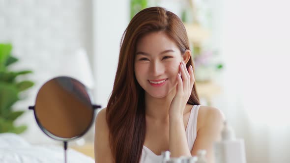 Happy Asian young woman smile and looking in mirror doing skin care touch cheek and beauty treatment