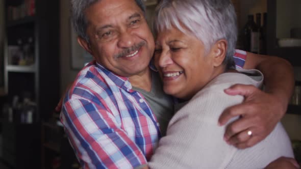 Happy senior mixed race couple smiling and embracing in kitchen