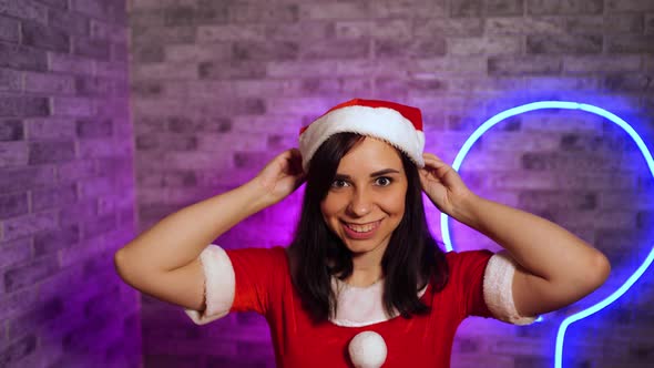 Young Woman in Santa Costume Puts on Christmas Hat