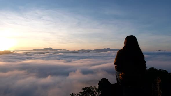 A female traveler sitting on the mountain peak, watching sunrise and sea of fog.