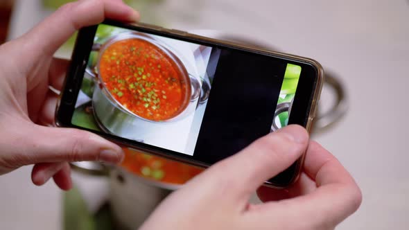 A Woman Looks at a Photo of Traditional Ukrainian Red Borscht on a Smartphone