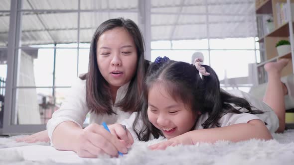 Happy Asian mom and her kid lying on the floor and drawing on paper together