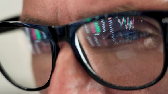 Trader Looking at Computer Screen Analyzing Trading Chart Reflecting in Glasses