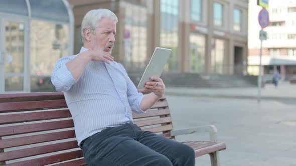 Old Man Reacting to Loss on Tablet While Sitting Outdoor on Bench