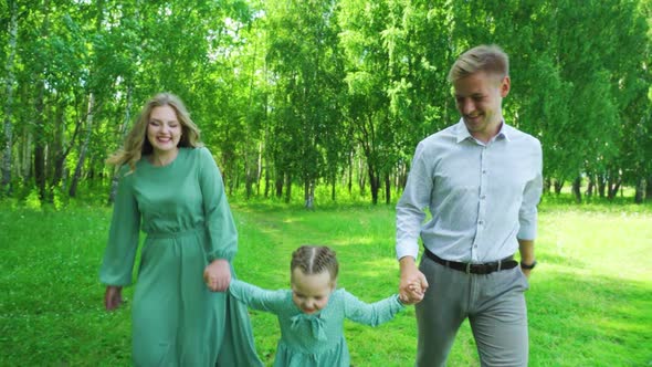 Young Family Holding Hands Running Through the Park in Summer