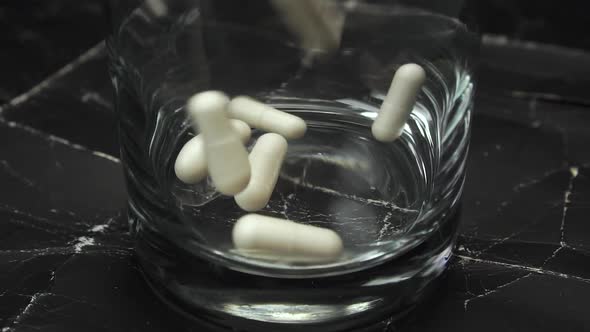 White medical capsules fall to the bottom of the glass 