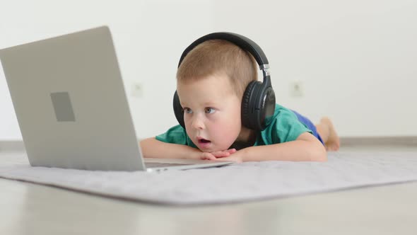 Little Child Kid Boy in Headphones Lying on Floor Looking Into Laptop Screen