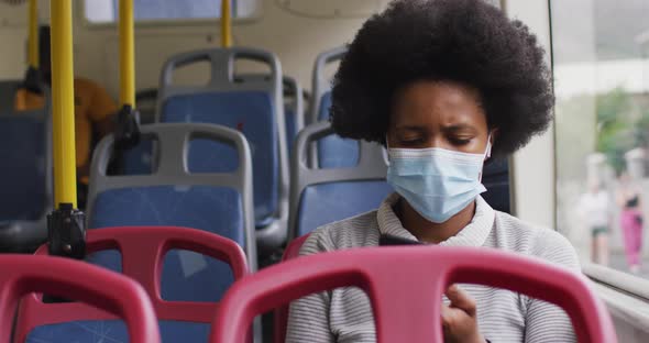 African american businesswoman with face mask using smartphone and sitting in bus