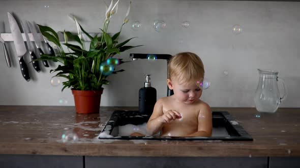 Cute Happy Baby Girl with Playing with Water and Foam in a Kitchen Sink at Home