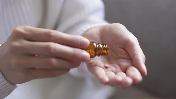 Close Up Young Woman Takes Medication. Several Pills Fall Into Woman's Hand From Bottle Of Pills