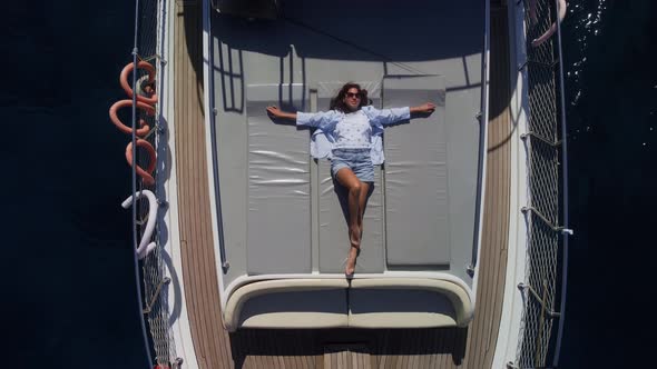 Young Caucasian Lady in Shorts and Shirt is Lying on the Deck of Private Yacht and Sunbathing