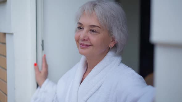 Cheerful Caucasian Mature Woman with Brown Eyes Smiling Standing at Doorway Looking Out