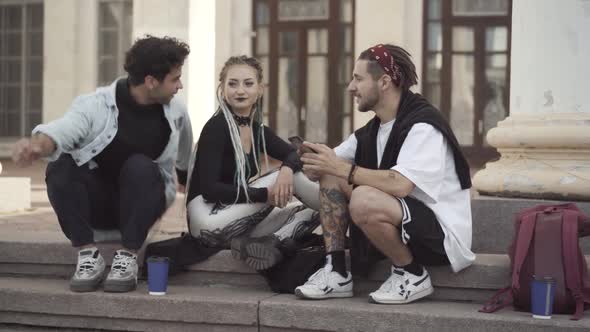 Couple of Hippies Sitting on Urban Stairs Greeting Friend