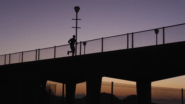 Silhouette of man running on bridge in the evening