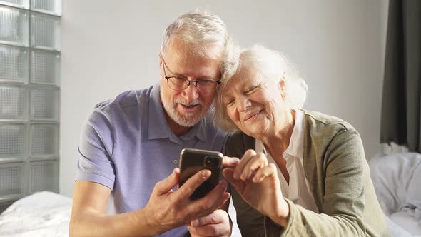 Funny Man and Woman of Retirement Age Using a Smartphone While Sitting at Home