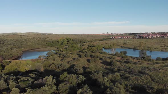 AERIAL Reverse Shot of a DAM in a Green Valley with Housing in the BACK