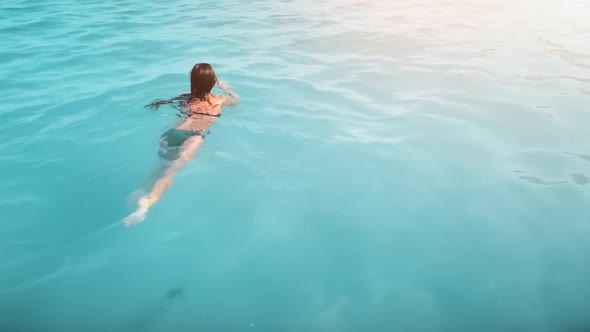 Aerial Slender Woman in Swimsuit Swims on Blue Sea View From Back