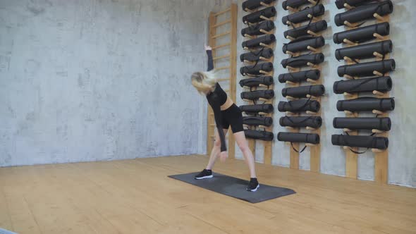 Young fit beautiful girl in black top, leggings, black sneakers doing joint stretching exercise