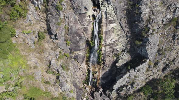 Small waterfall falling on rocky cliff. Mizarela cascade, Portugal. Aerial view, tilt up