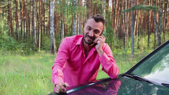 Smiling Businessman Speaks on the Phone Leaning on the Hood He is Happy