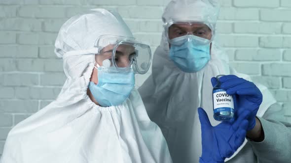 Male Scientist in a Protective Suit Passes a Covid-19 Vaccine To His Colleague. New Medication