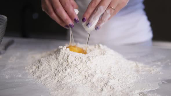 Closeup View of Female Hands Breaking the Egg Into Flour on the Kitchen Table