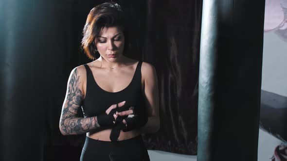 Tattooed Woman Binding Her Hands and Stands in the Fighting Pose  Looking in the Camera