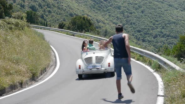 Four friends in convertible driving past hitchhiker