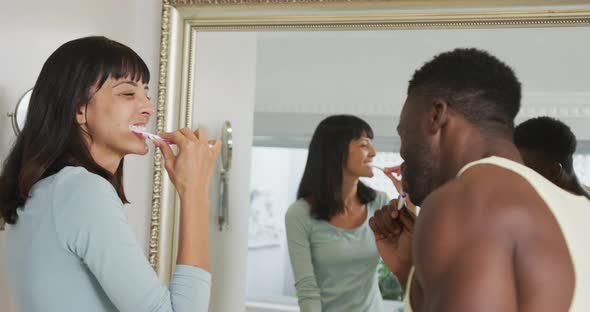 Happy diverse couple looking in mirror and brushing teeth in bathroom