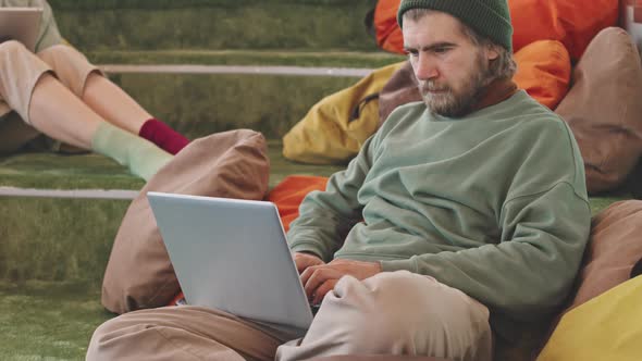 Hipster Working on Laptop in Lounge Area of Coworking Space