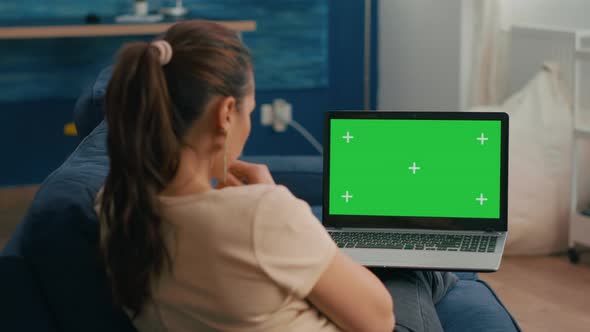 Freelancer Woman Sitting on Sofa in Home Office Typing on Laptop Computer with Mock Up Green Screen