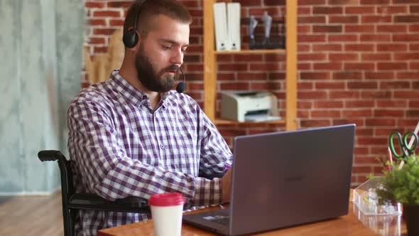 Man is Sitting in Wheelchair Using Laptop with Headset Talking Via Video Link and Recording