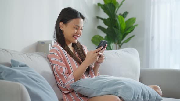 Asian beautiful woman sit on sofa and chat on mobile phone in house.