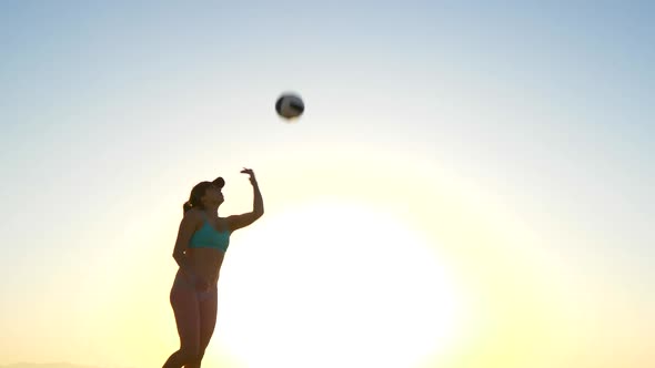 Women players play beach volleyball and a player jump serves serving the ball.